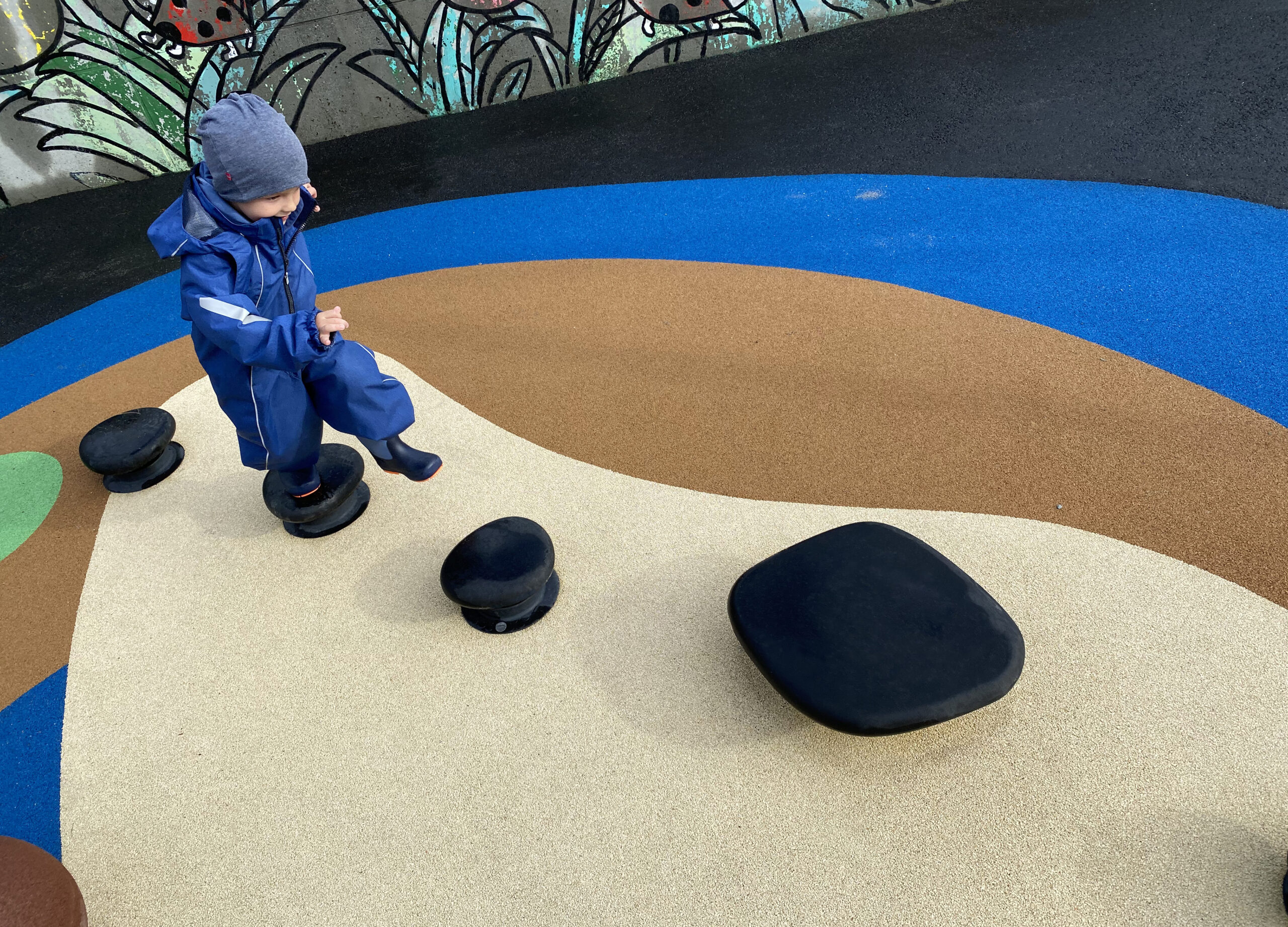 liten gutt som leker på hoppesteiner satt i løype på lekeplass i barnehage, liten gutt løper og leker i hinderløype, sula kommune, FUS-barnehage