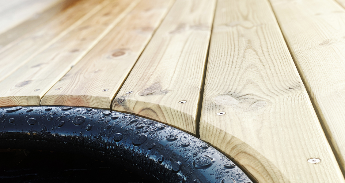 Nærbilde av kant for trampoline, overgang mellom trampoline og fallunderlag av tre, ShockDeck dempende fallunderlag for lekeplasser